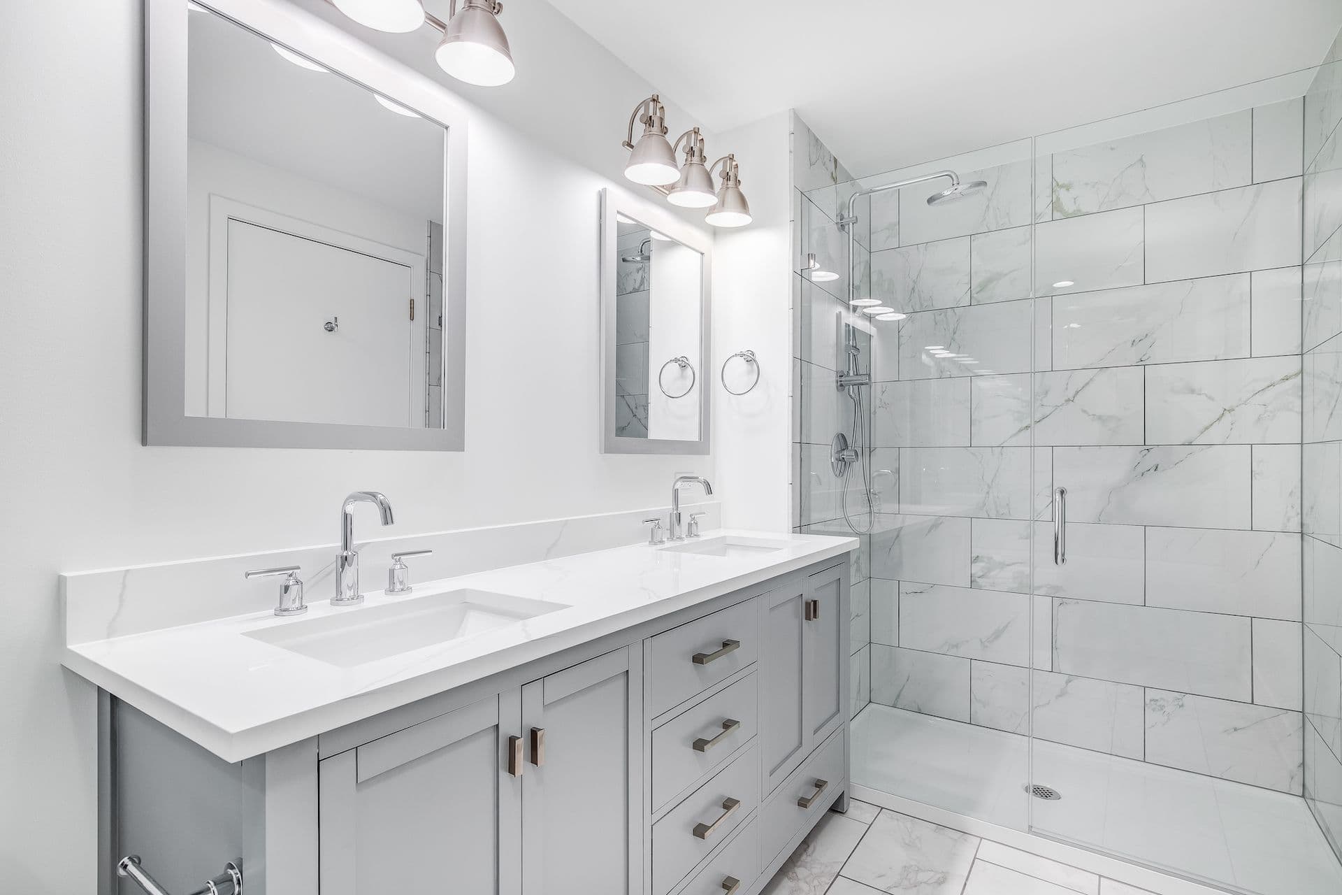 Modern bathroom with a sleek, dual-sink vanity, a large glass-enclosed shower, and white marble tiles.
