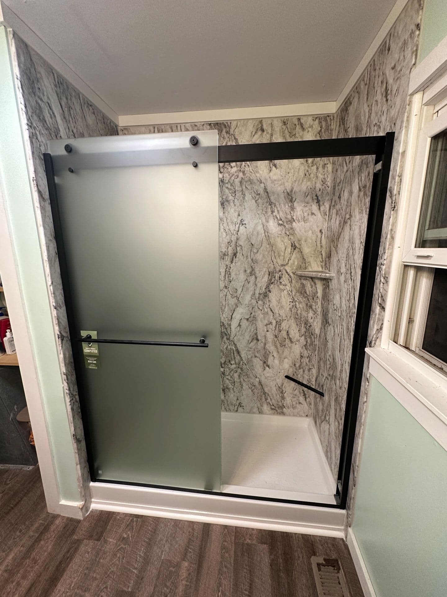 Modern bathroom featuring a frameless glass shower with frosted sliding door, marble-patterned walls, and dark hardware.