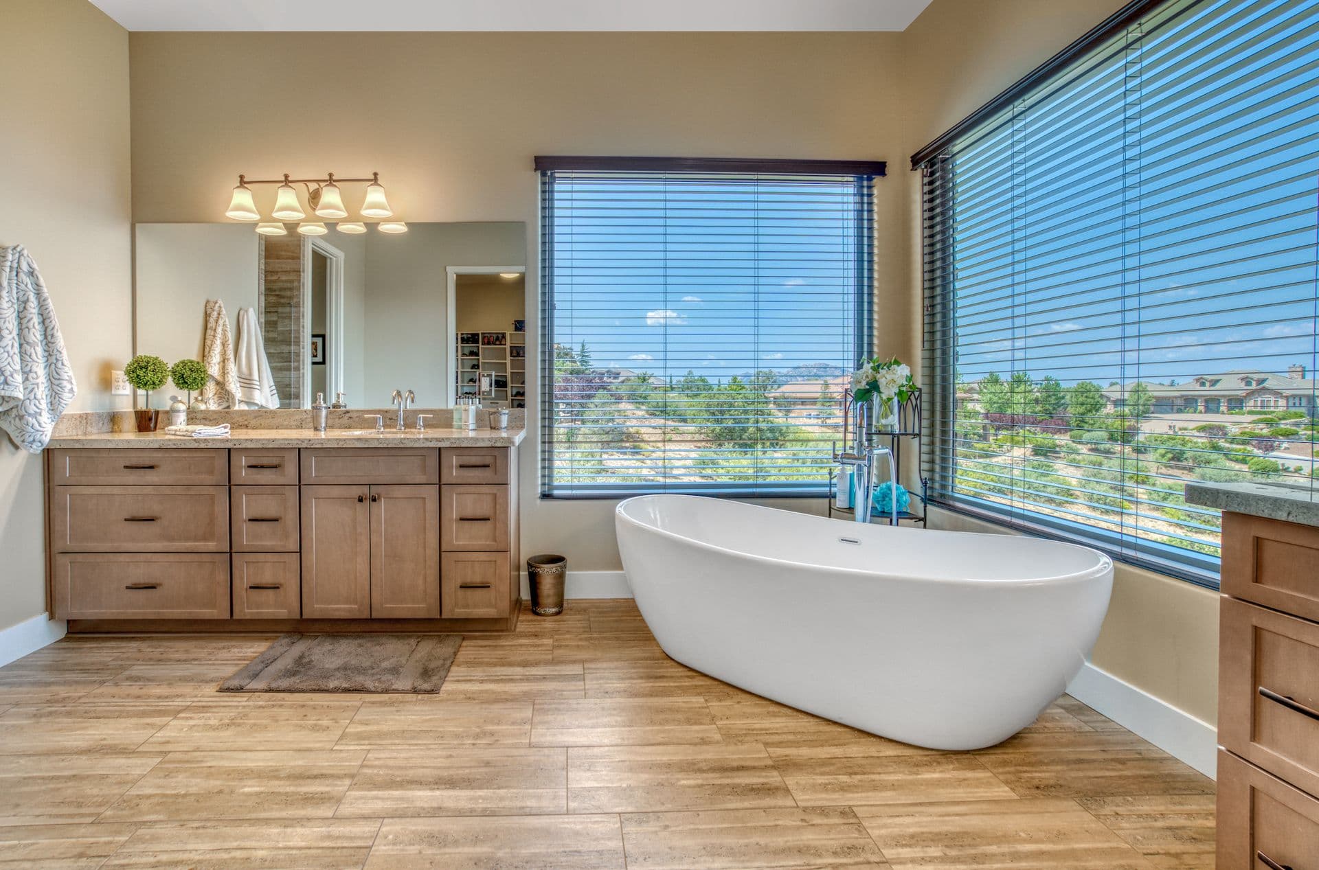 A tan bathroom with two large corner picture windows and a white soaking tub.
