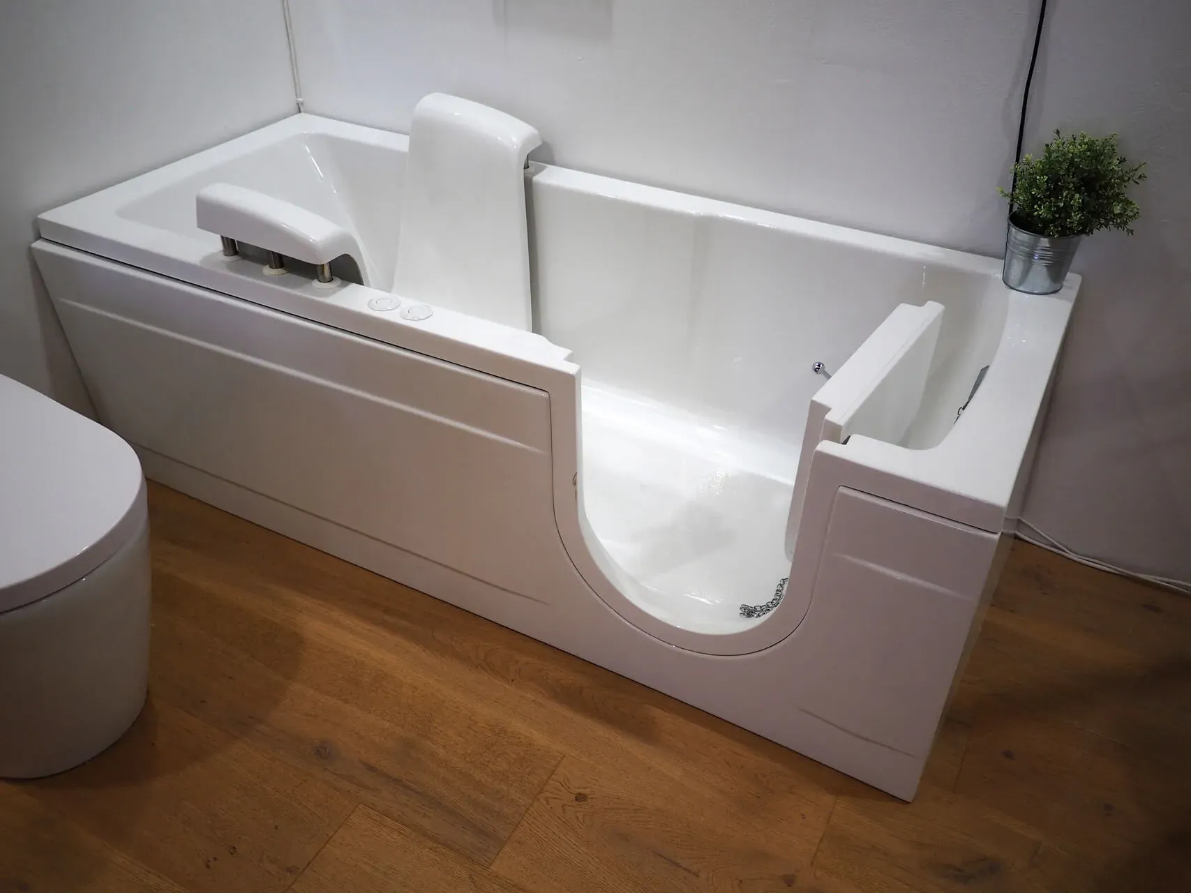 Accessible white bathtub with a side door for easy entry, placed in a modern bathroom with wood floors and a small plant nearby.