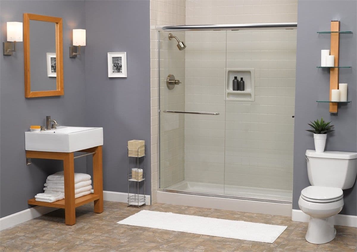 Modern bathroom with gray walls, glass shower, toilet, wooden vanity with sink, mirror, white towels, and shelves with candles and plant.