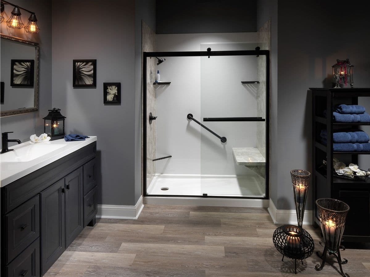 A gray bathroom with a walk-in shower with sliding glass doors, black fixtures, diagonal grab bar, and built-in shower bench seat.