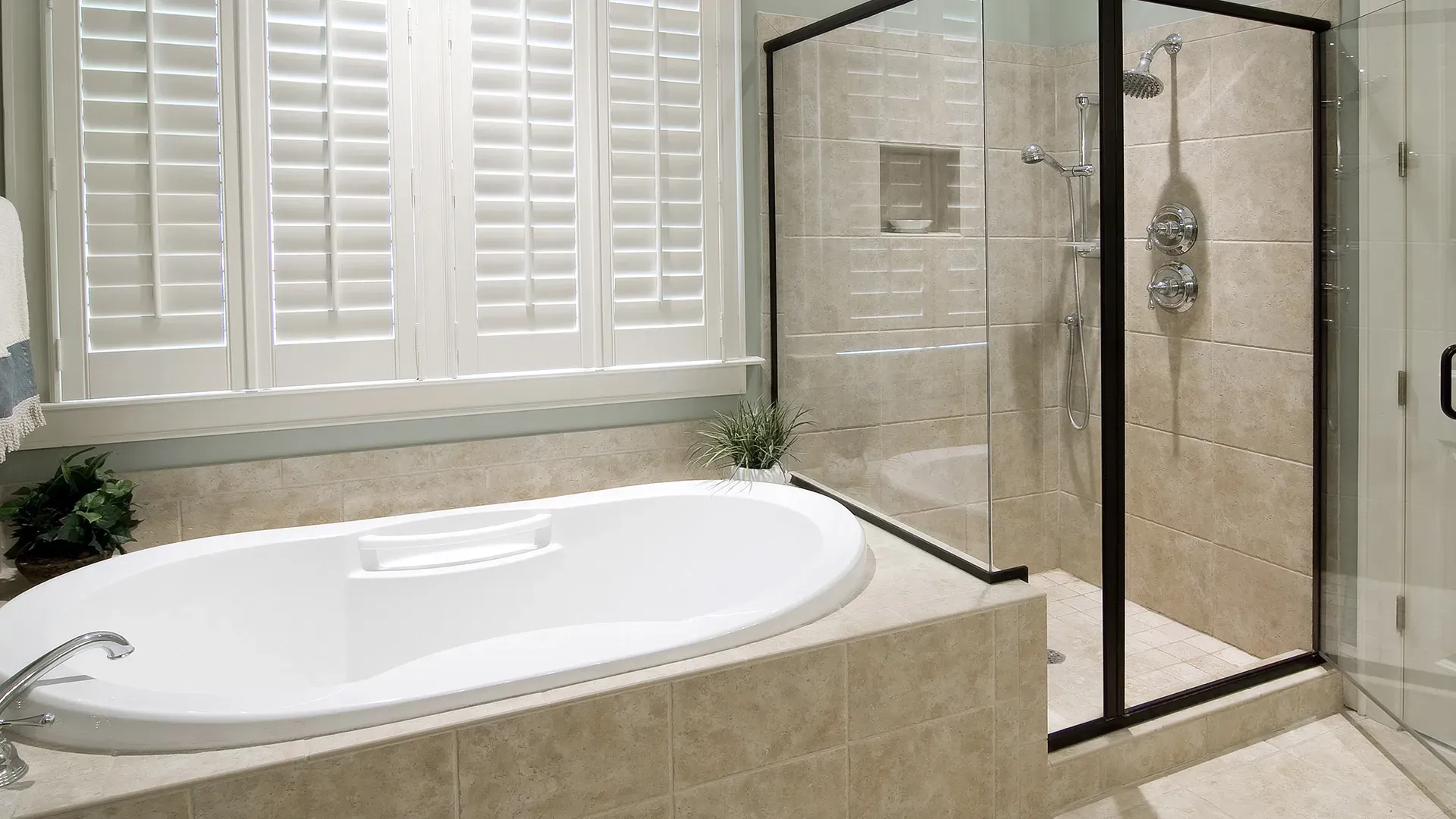 A modern bathroom features a white oval soaking bathtub beside a glass-enclosed shower with beige tiles.