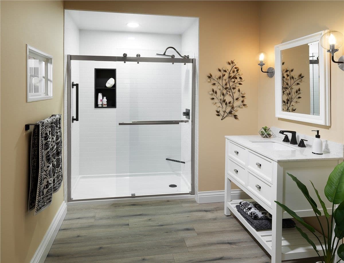 A beige bathroom with a converted walk-in shower with white tile walls and sliding glass doors.