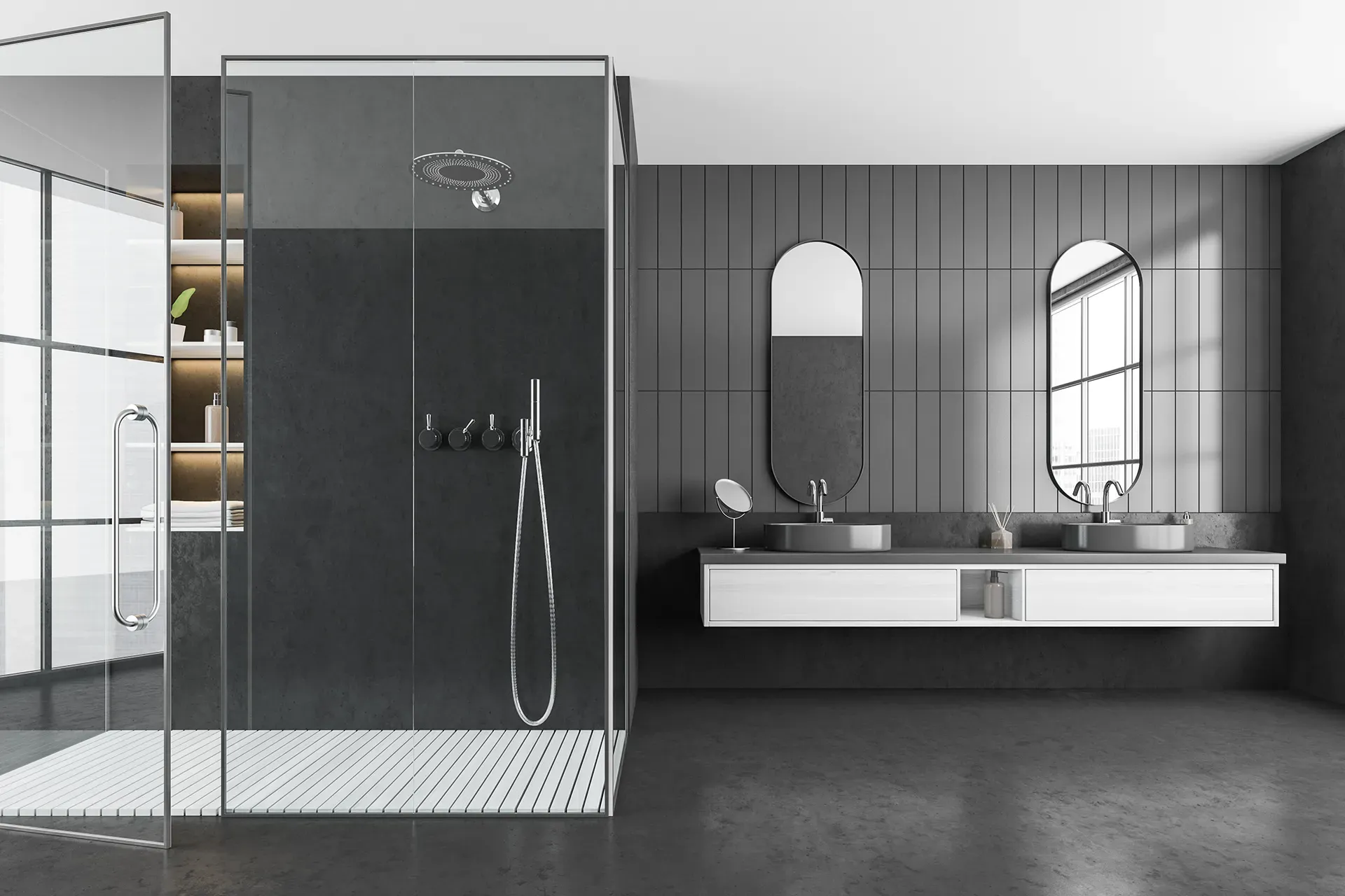 A sleek, modern bathroom with a glass shower enclosure on the left, dark walls, two oval mirrors above a dual sink vanity, and soft natural light.