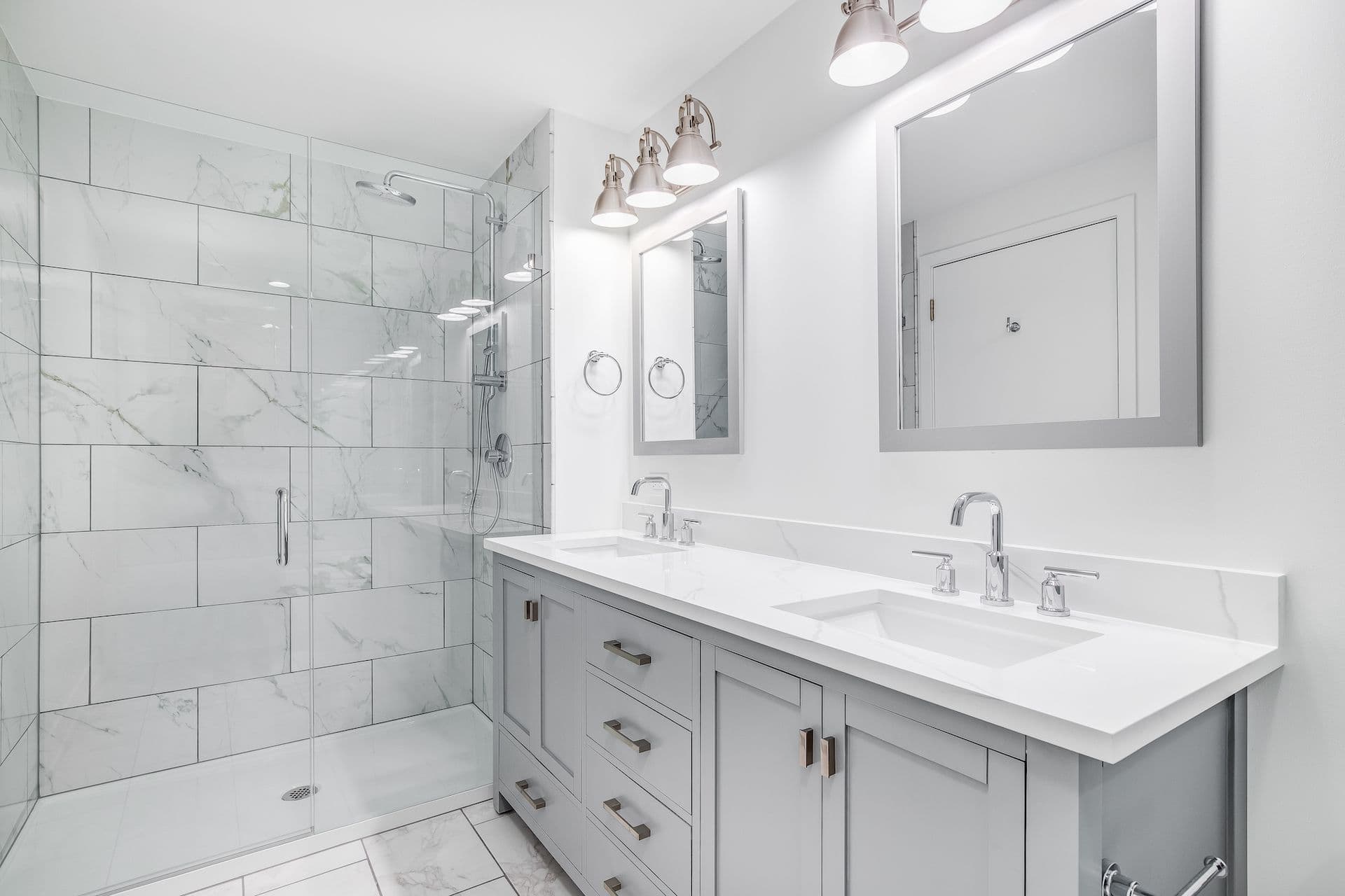 Modern bathroom with a sleek, dual-sink vanity, a large glass-enclosed shower, and white marble tiles.